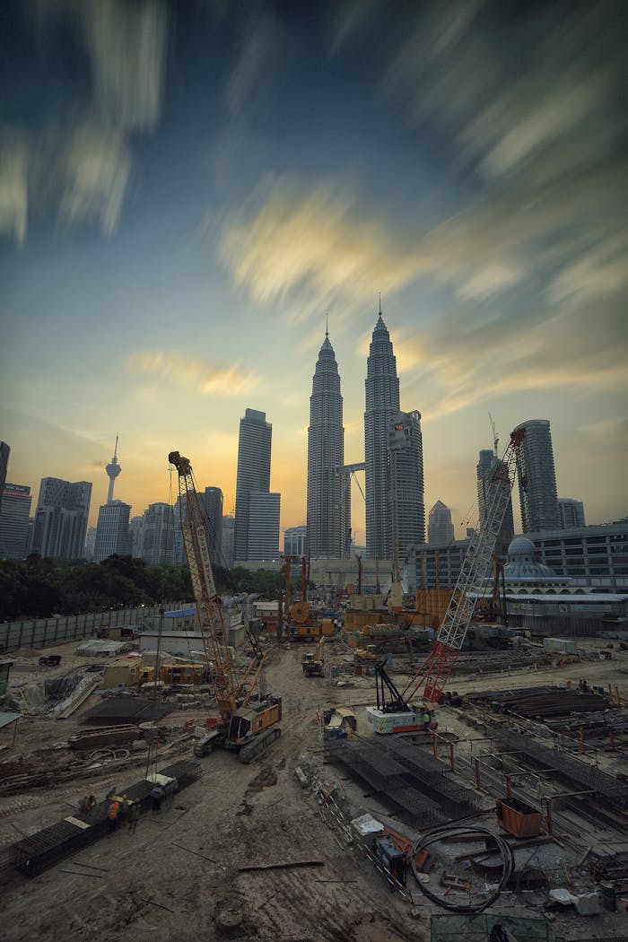 Dramatic view of the Petronas Towers towering over a busy construction site in Kuala Lumpur at sunset.